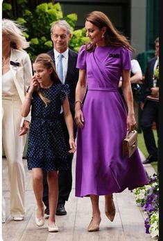 a woman in a purple dress walks with two small girls and an older man behind her