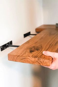 a hand is holding the edge of a wooden table with two black brackets on it