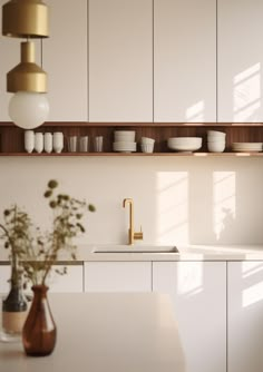 a kitchen with white cabinets and gold faucet on the counter top next to a vase filled with flowers