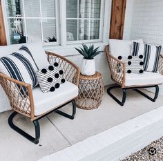 two wicker chairs with black and white pillows sitting on the front porch next to each other