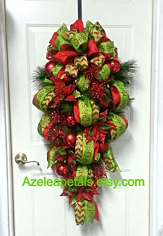 a green and red christmas wreath hanging on the front door with ribbons, bows and ornaments