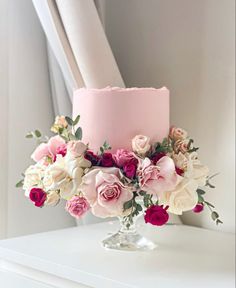 a pink cake with white and red flowers on the top is sitting on a table