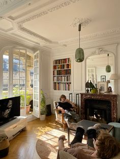 two people are sitting in a living room with bookshelves and a fire place