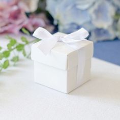 a small white box with a bow on it sitting next to some flowers and greenery