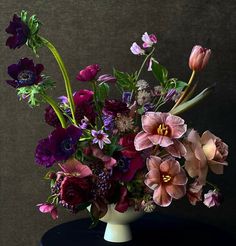 a white vase filled with lots of purple and pink flowers on top of a table