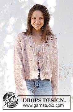 a woman wearing a pink cardigan standing in front of a white wall with the words drops design on it