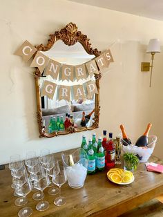 a wooden table topped with lots of wine glasses and bottles next to a wall mounted mirror