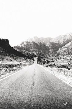 a black and white photo of an empty road with mountains in the backgroud