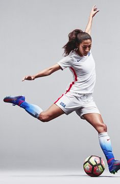 a woman kicking a soccer ball on top of a white field covered in blue and red