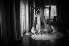 a bride's wedding dress hanging in front of a window with shoes on the floor