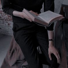 a woman sitting on a bed holding an open book in her lap and reading it