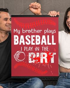 a man and woman holding up a sign that says, my brother plays baseball i play in the dirt