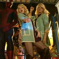 two women are standing in front of a spider man and another woman is holding her hand out