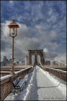 a bench sitting on the side of a bridge covered in snow next to a street light