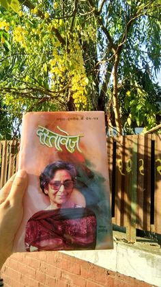 a person holding up a book in front of a tree