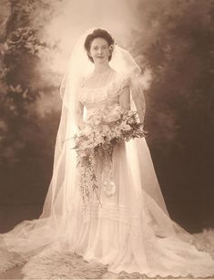 an old photo of a woman in a wedding dress and veil holding a bouquet of flowers