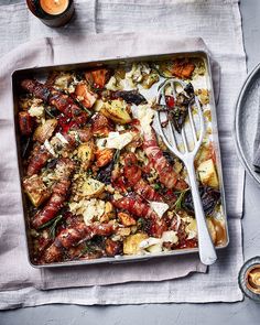 a pan filled with meat and vegetables on top of a table next to utensils