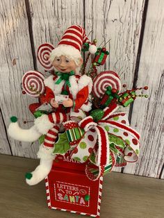 a small christmas decoration with candy canes and santa clause on the top, sitting in front of a wooden wall