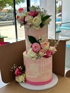 a three tiered cake with pink and white flowers on the top is sitting on a cardboard box