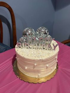 a birthday cake sitting on top of a pink tablecloth covered table with disco balls