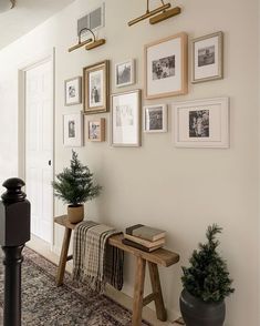 a hallway with pictures on the wall and a wooden bench in front of some potted plants