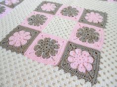 a crocheted blanket with pink and gray flowers on it, sitting on top of a bed