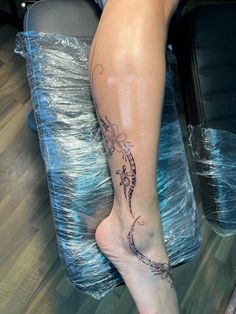 a woman's leg with a tattoo on it sitting in front of a chair