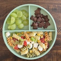 a green bowl filled with pasta and veggies on top of a wooden table