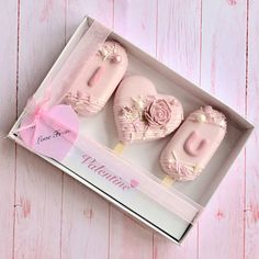 three pink heart shaped cookies in a box on a table with a ribbon around the edges