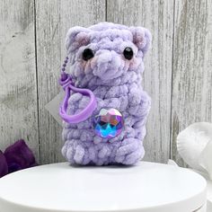 a purple teddy bear with a keychain on it's back sitting on top of a white stool