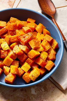 a blue bowl filled with cut up sweet potatoes on top of a table next to a wooden spoon