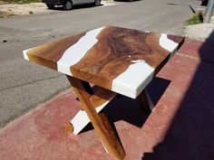 a wooden table sitting on the side of a road next to a parking lot with cars parked in front of it