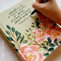 a hand holding a pen writing on top of a notebook with flowers painted on it