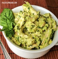 a white bowl filled with broccoli salad on top of a wooden table next to a green leafy garnish