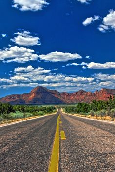 an empty road in the desert with mountains in the backgrouund and clouds in the sky