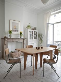 a dining room table and chairs in front of a fireplace with potted plants on it