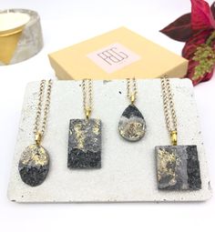 three pieces of jewelry sitting on top of a white table next to a box with gold foil