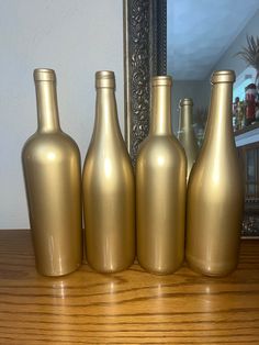 four gold colored vases sitting on top of a wooden table next to a mirror