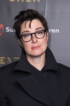 a woman wearing glasses standing in front of a sign