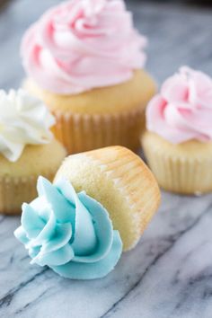 three cupcakes with pink, blue and white frosting sitting on a marble surface