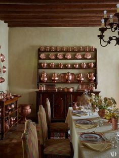 a dining room table set with place settings and copperware on the wall behind it