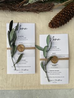 the wedding stationery is laid out with pine cones and greenery, as well as an olive branch