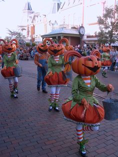 several people in costumes are walking down the street with pumpkins on their heads and legs