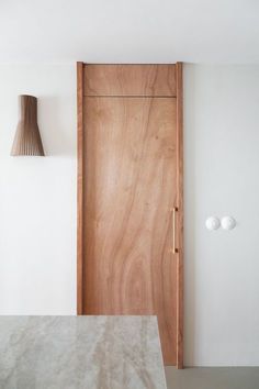 a wooden door in a white room next to a table with a lamp on it