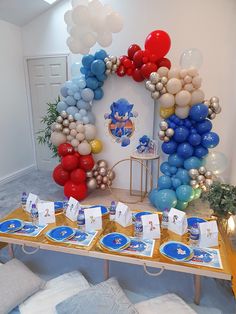 a table topped with balloons and plates on top of a wooden table next to a white wall