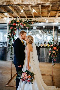 a bride and groom kissing in front of an arch decorated with floral garlands at their wedding