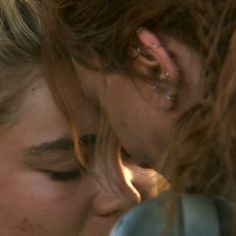 two women are kissing each other with their noses close to one another, both wearing ear rings