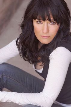 a woman sitting on the ground with her hands in her pockets and looking at the camera