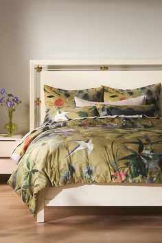 a bed with floral comforter and pillows on top of it, next to a night stand