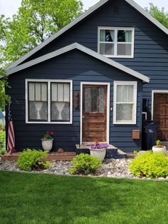 a blue house with flowers in front of it and an american flag on the lawn